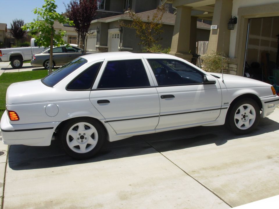 White sedan parked in driveway, another car and truck in background
