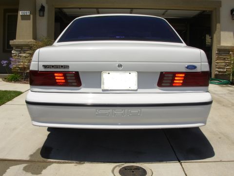1995 Ford Taurus - Rear view of a white Ford Taurus SHO parked in a driveway, showing its distinctive taillights and badging.