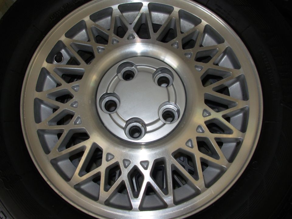 Aluminum alloy wheel with a complex geometric spoke pattern, showing lug nuts and part of a tire