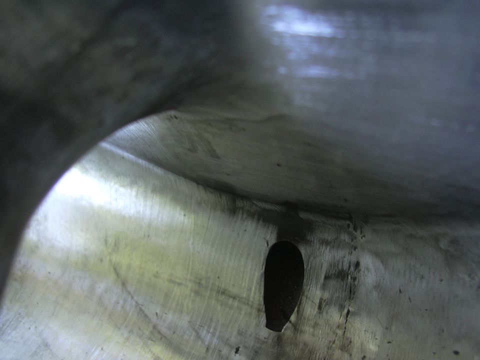 Engine intake plenum with a hole, showing brushed metal texture and dark interior