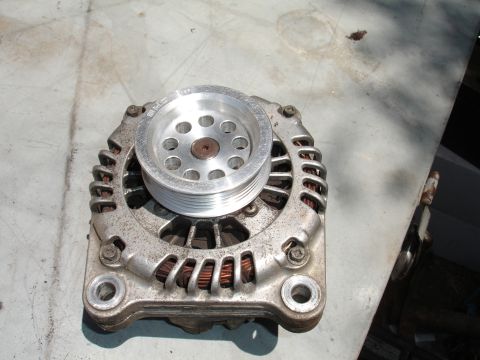 1993 Ford Taurus - Close-up of a car alternator with a multi-groove pulley, resting on a textured surface.