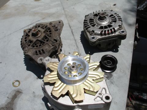 1993 Ford Taurus - Three alternators, one with a gold fan, and a pulley are laid out on a workbench.