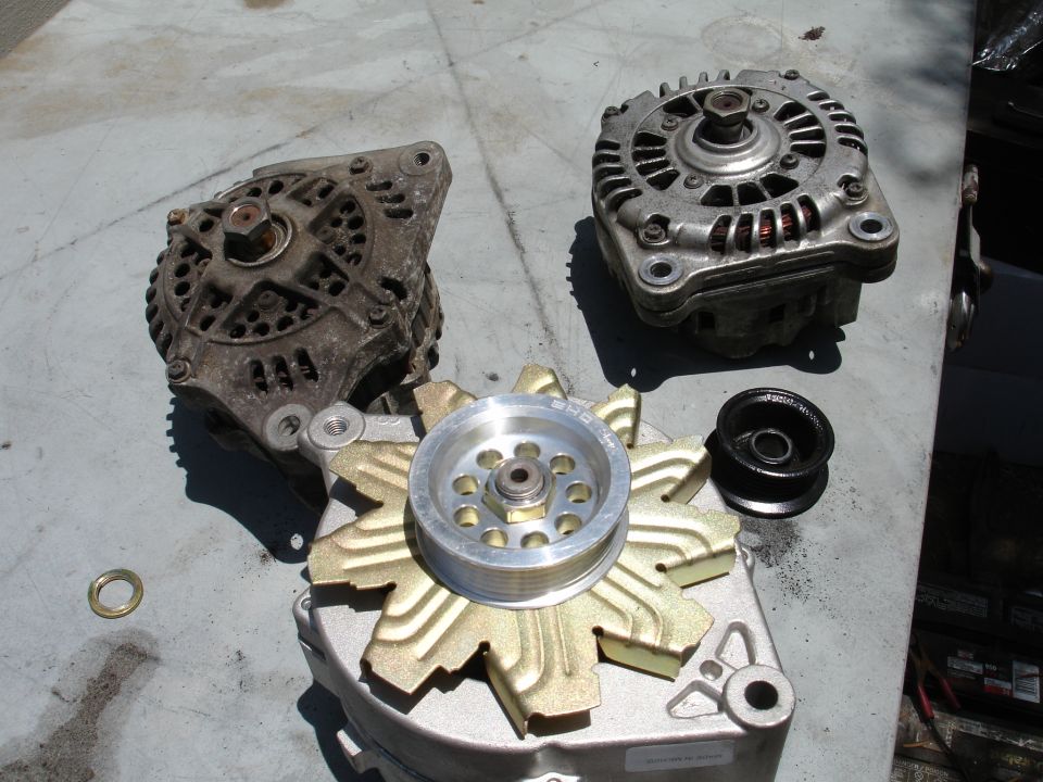 Three alternators and a pulley on a workbench. One alternator has a gold fan