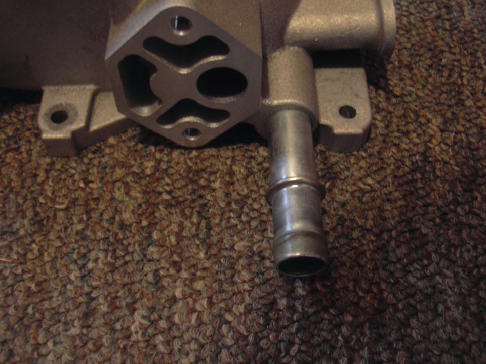 Close-up of a metal automotive part with a hose barb, resting on a brown carpet
