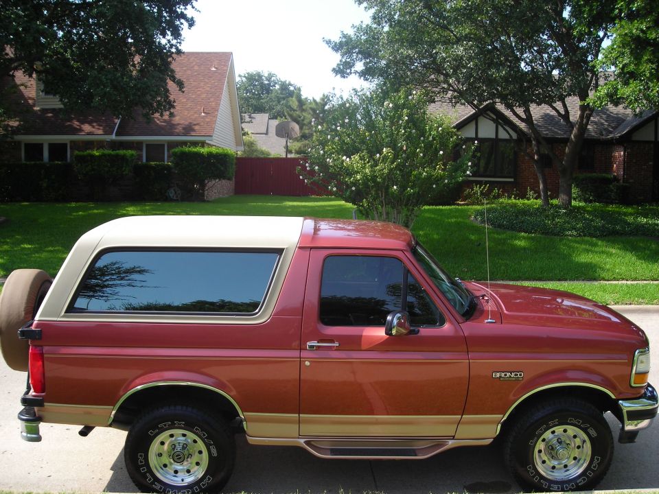 Red and tan Ford Bronco SUV, side view, spare tire on rear door, parked in residential area