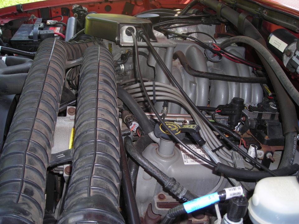 Engine bay with dual air intake hoses, distributor cap, and intake manifold. Some text visible on engine parts