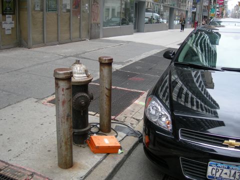 1992 Ford Taurus - A black car is parked on a city street next to a fire hydrant and bollards, with building reflections visible on its hood.