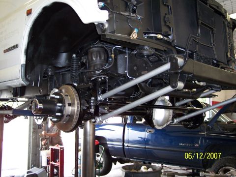 1996 Ford Bronco - The undercarriage and suspension of a white truck are shown, with a blue pickup truck in the background.