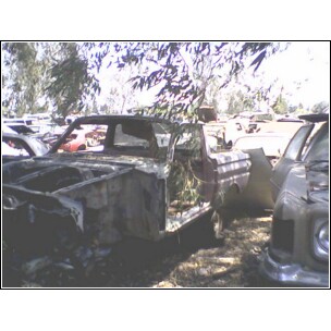1973 Ford Ranchero - A stripped-down car chassis sits in a junkyard, showing its open door and damaged front.