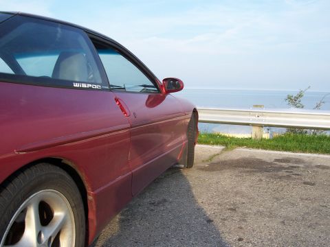 1995 Ford Probe - Side profile of a red 1995 Ford Probe GT parked next to a guardrail with a water view.