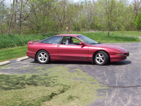 1995 Ford Probe - A red 1995 Ford Probe is parked in a lot with trees and grass in the background.