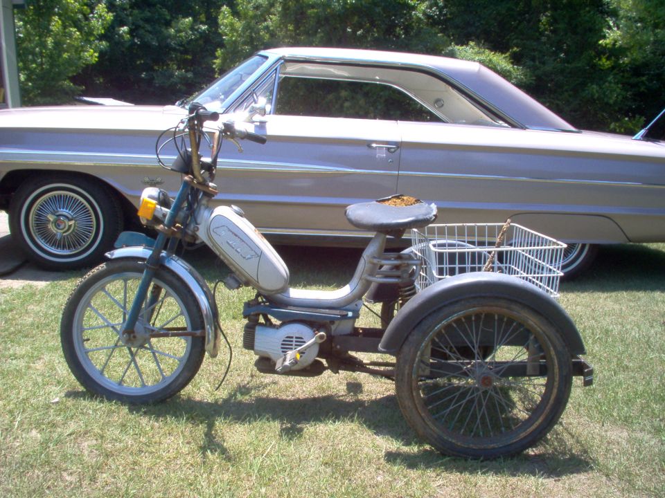 Side view of a vintage car with a three-wheeled moped in front
