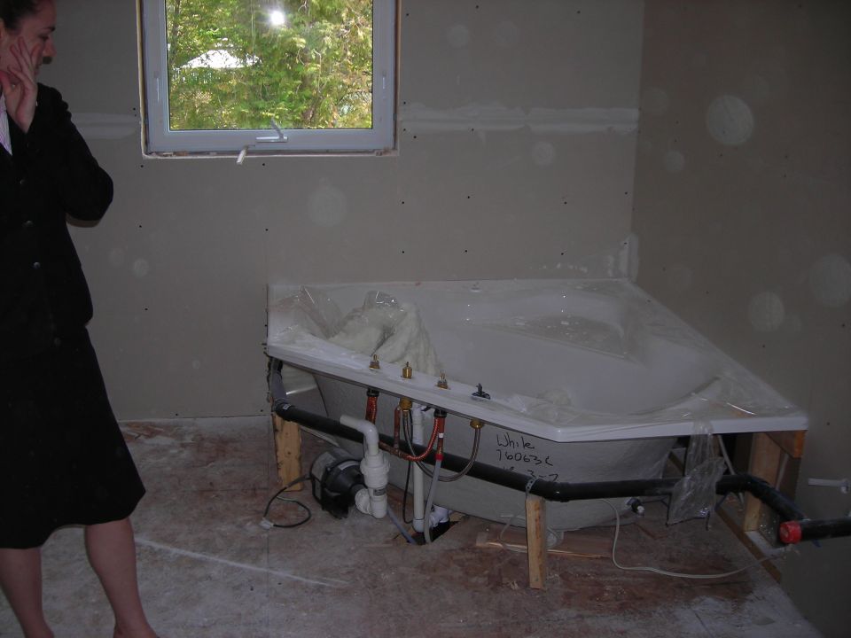 Bathtub with plumbing, a woman in a black suit stands to the left