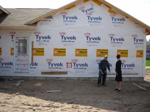 1984 Ford Bronco - Two people stand on a dirt lot in front of a house under construction, covered in Tyvek wrap.