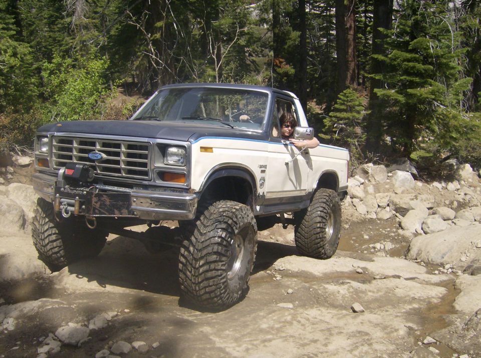 Ford Bronco with large tires driving on a rocky trail in the woods
