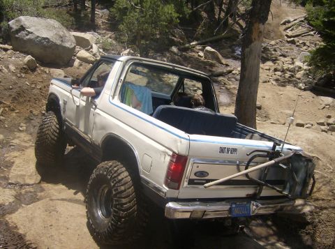 1986 Ford Bronco - White 1986 Ford Bronco navigating a challenging off-road trail with large tires.