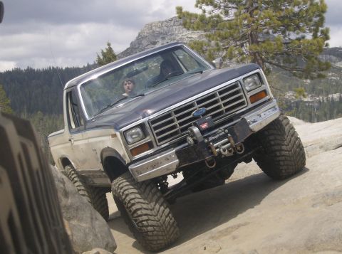 1986 Ford Bronco - A two-tone Ford Bronco navigates a rocky trail with a winch mounted on the front bumper.