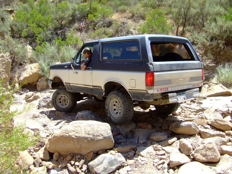 Two-tone 1987 Ford Bronco navigating a rocky trail