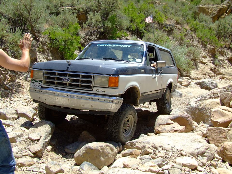 1987 Ford Bronco navigating a rocky trail, front passenger side visible, hand waving from driver's window
