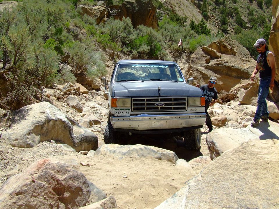 1987 Ford Bronco navigating a rocky trail with two people standing nearby