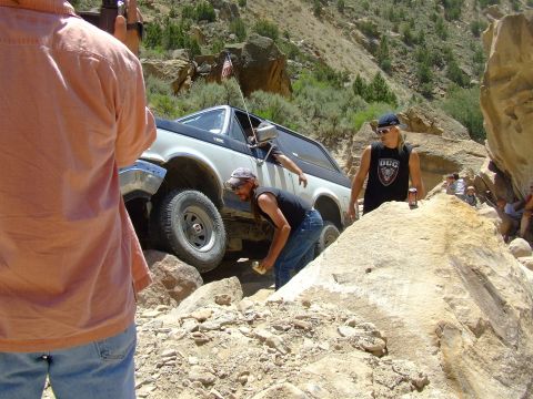 1987 Ford Bronco - A two-tone Ford Bronco tackles a challenging off-road course with spectators observing the action.