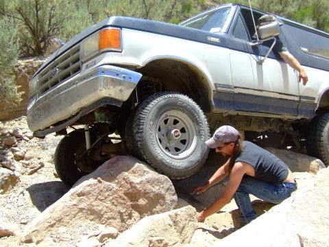 1987 Ford Bronco - Ford Bronco tackling a difficult off-road obstacle, with a person assisting.