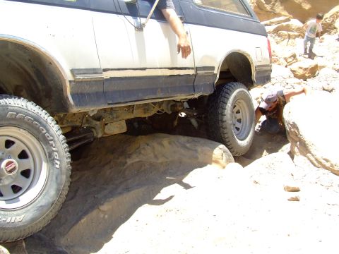 1987 Ford Bronco - A 1987 Ford Bronco is shown off-roading over large rocks, with a person leaning out of the driver's side window.