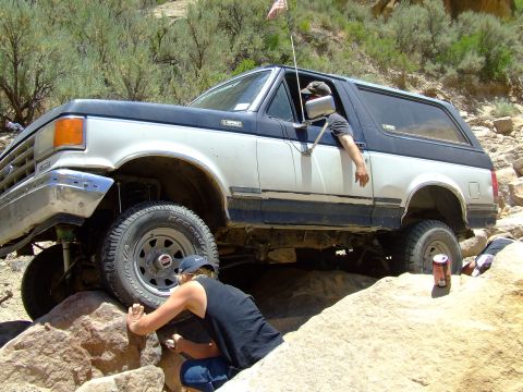 1987 Ford Bronco - A 1987 Ford Bronco navigates a rocky trail with a person assisting from outside.