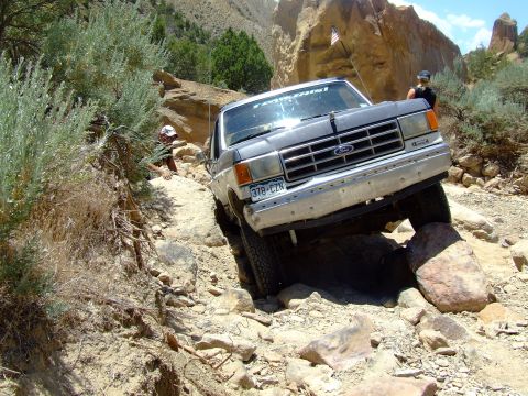 1987 Ford Bronco - Ford Bronco tackling a challenging rocky trail, with a person watching from the side.