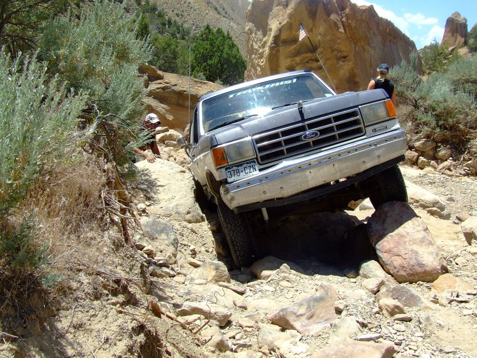 1987 Ford Bronco navigating a rocky off-road trail with a person visible in the background