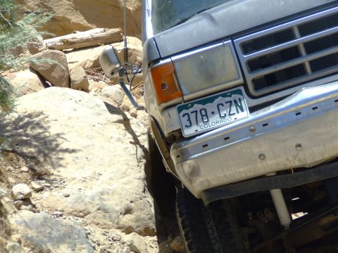 1987 Ford Bronco - A 1987 Ford Bronco is shown on a challenging off-road path with large rocks and steep inclines.