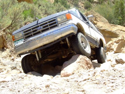 1987 Ford Bronco - 1987 Ford Bronco tackles a challenging off-road trail with large rocks.