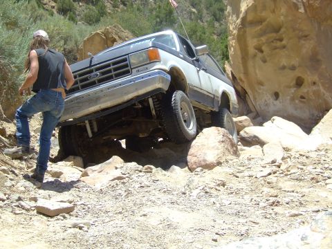 1987 Ford Bronco - A person walks near a Ford Bronco as it drives over rocks on a trail.