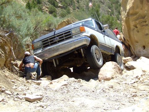 1987 Ford Bronco - A Ford Bronco tackles a challenging off-road course with a person adjusting rocks in front of it.