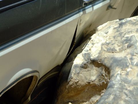 1987 Ford Bronco - A vehicle's side panel is severely damaged and caught on a large rock.
