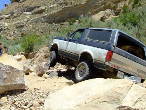 1987 Ford Bronco - A two-tone 1987 Ford Bronco tackles a challenging rocky terrain on an off-road adventure.