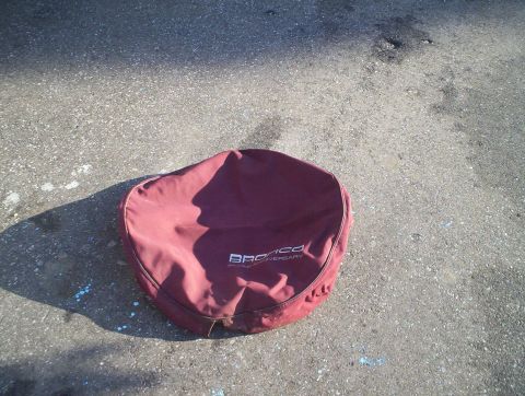 1991 Ford Bronco - A maroon spare tire cover with "BRONCO 25th ANNIVERSARY" text lies on the ground.