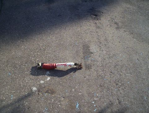 1991 Ford Bronco - A Rancho RSX shock absorber with red bellows lies on an asphalt surface.