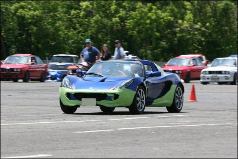 2001 Mercury Grand Marquis - A blue Lotus Elise with green tape on its front and sides is seen on a race track with other vehicles in the background.