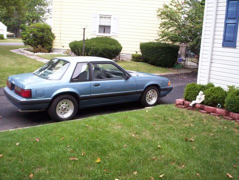 1991 Ford Bronco - A blue coupe is parked on a driveway next to a house. The vehicle appears to be a 1991 Ford Mustang.