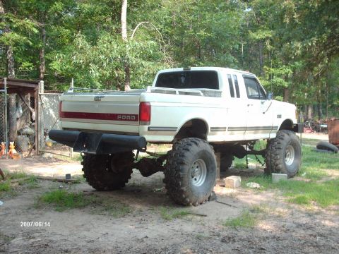 1990 Ford F-150 - A white pickup truck modified with a flatbed and oversized rear wheels is seen outdoors.