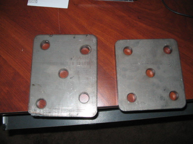 Two square metal plates with four bolt holes each, on a wooden surface