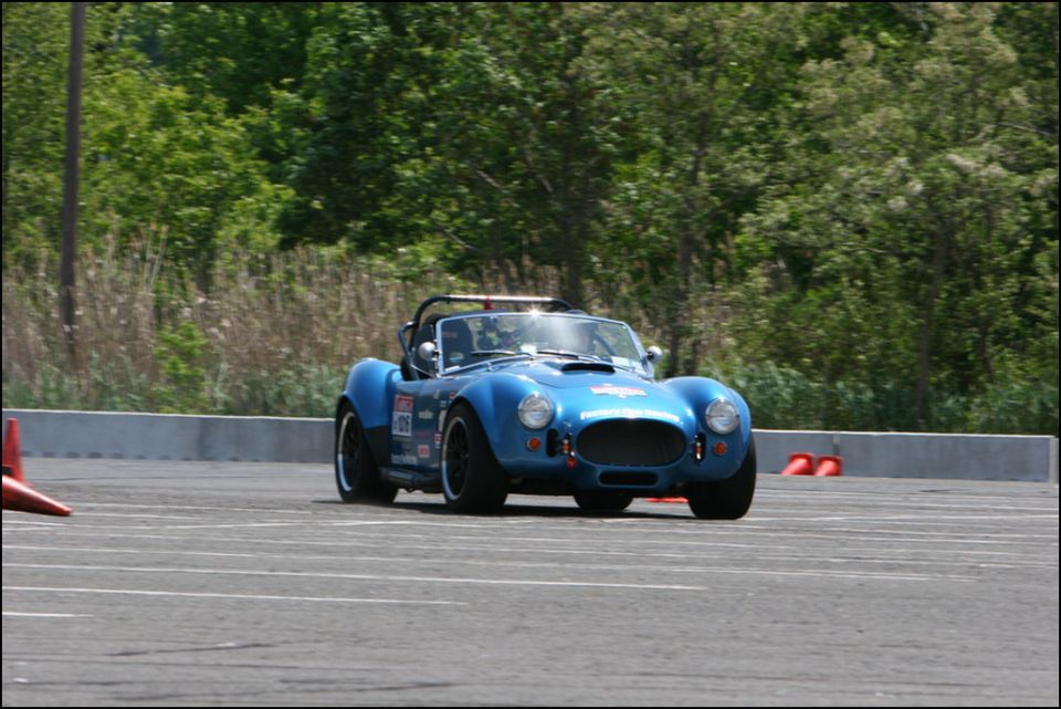 Blue AC Cobra replica on a race track, driver visible inside. Number 09 on door