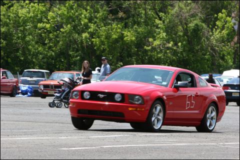2001 Mercury Grand Marquis - A red Ford Mustang with racing numbers is parked in a lot with other vehicles and people.