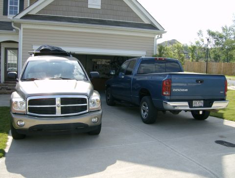 2004 Dodge Durango - Two Dodge vehicles, a Durango SUV and a Ram pickup, are parked in front of a suburban garage.