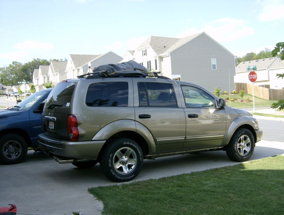 Tan Dodge Durango SUV, 3/4 rear, loaded roof rack, blue Ram pickup alongside driveway
