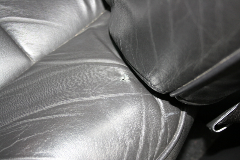 Black leather car seat interior with a small tear on the lower cushion