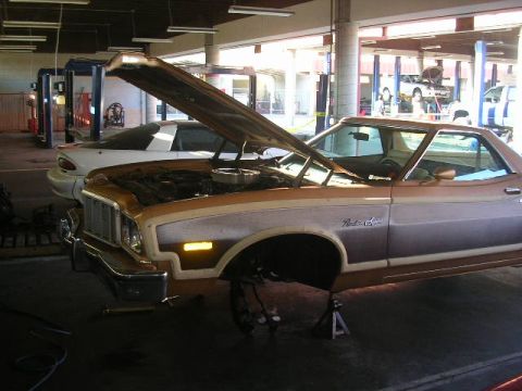 1975 Ford Ranchero - A 1975 Ford Ranchero is undergoing repairs in a garage, with its hood up and front wheel off.