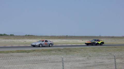 1990 Ford Probe - Two cars compete on a race track under a clear blue sky.