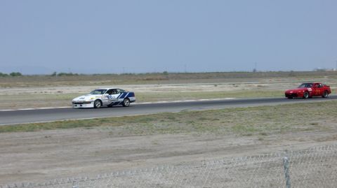 1990 Ford Probe - A white and blue race car speeds along a track, with a red car in the distance.